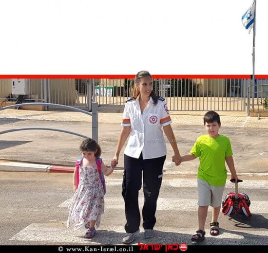אשת צוות מגן דוד אדום עם שני תלמידי כיתה א' חוצים את הכביש בביטחה | צילום: דוברות מדא | עיבוד צילום ממחושב: שולי סונגו©