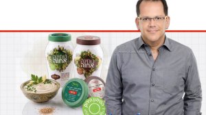 יובל מלאך, סמנכ"ל השיווק והמכירות של חב' אחוה, צנצנות טחינה גולמית של "אחוה המכסים פונים קדימה ומציגים בבירור המדבקות החדשות והסימון הירוק של משרד הבריאות | עיבוד: Gemini Google | עיצוב: שולי סונגו©