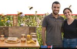 זוג צרכנים עם צנצנת דבש מוזהבת לצד כפפת עץ ייעודית לדבש ותפוחים אדומים על שולחן עץ כפרי | עיבוד: Gemini Google | עיצוב: שולי סונגו©